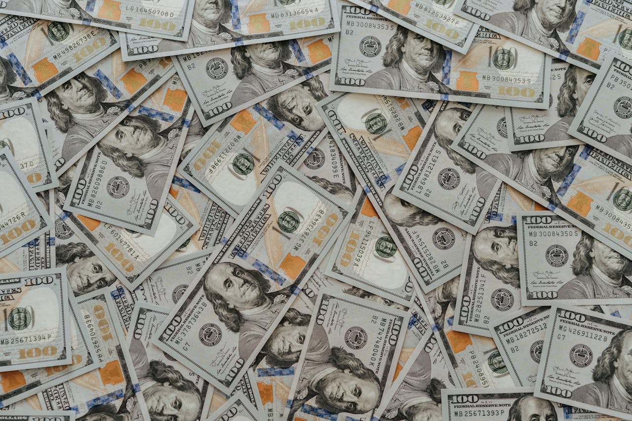 gallery-02 US hundred dollar bills scattered in abundance creating a financial backdrop.