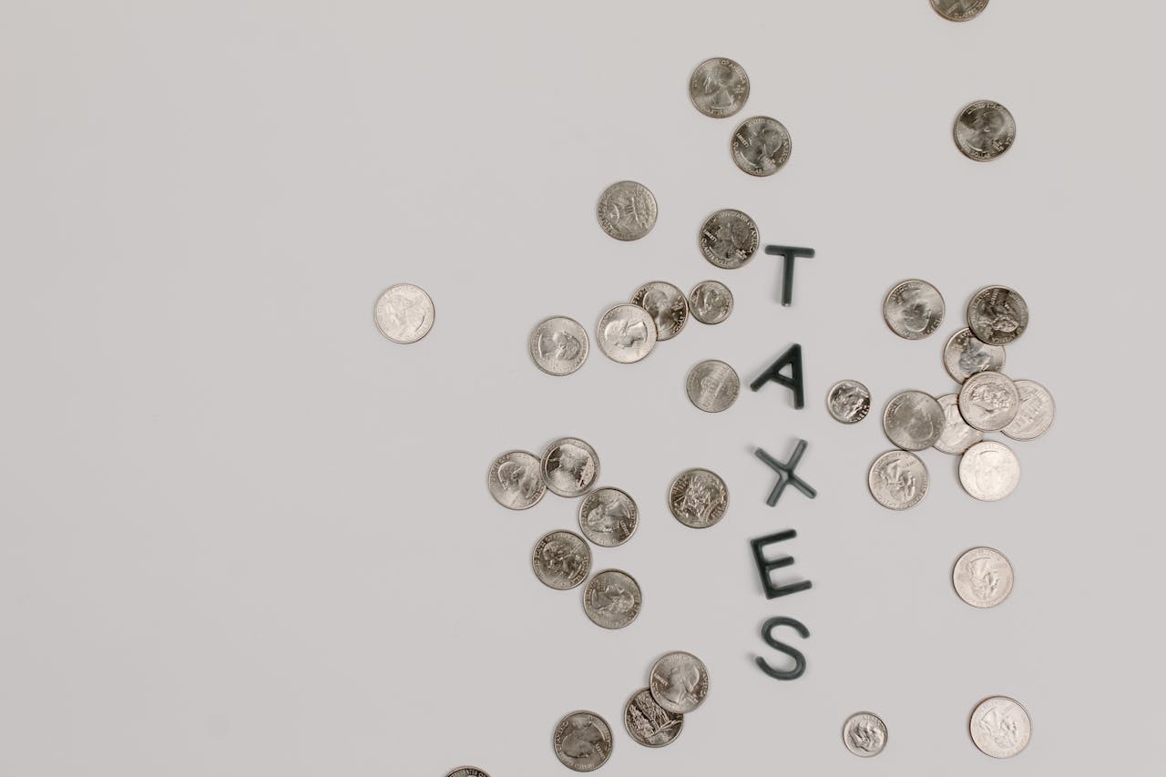gallery-03 Scattered coins forming the word 'TAXES' on a white surface, symbolizing financial concepts.